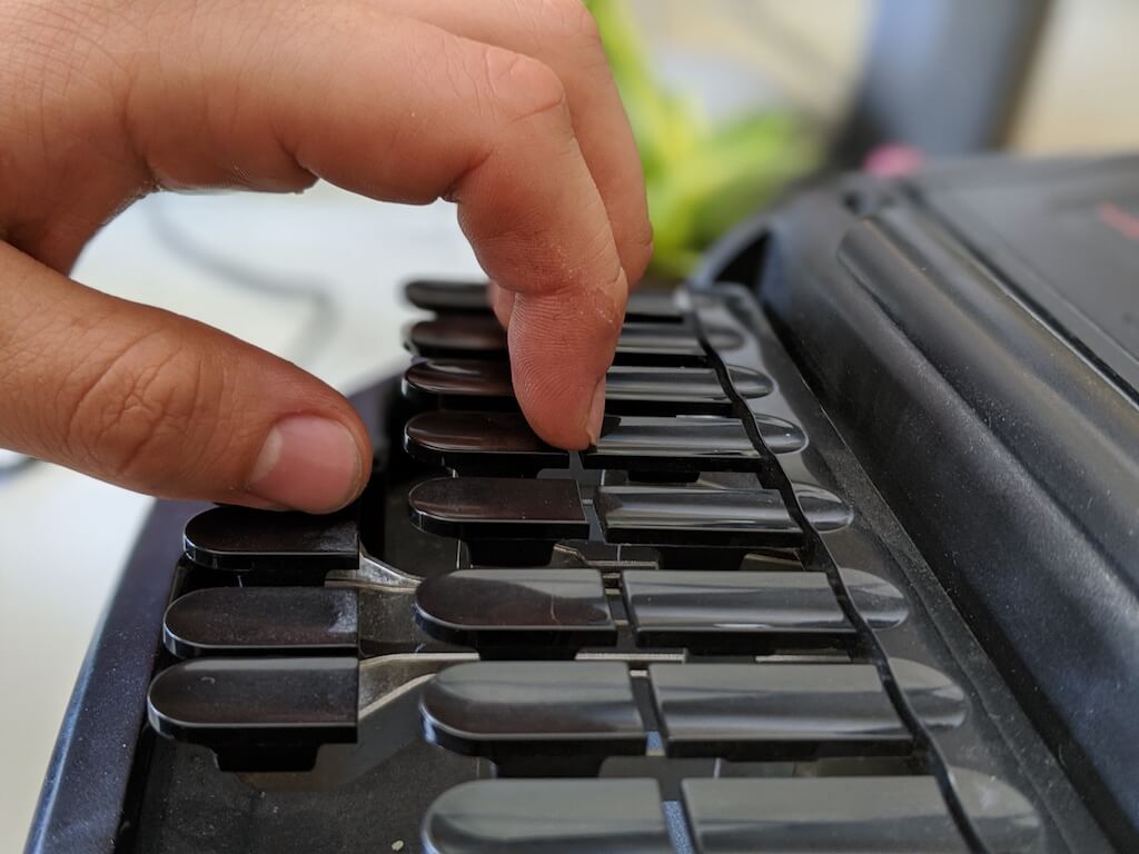Stenographer curling their left-hand fingers onto the cracks of a steno machine's keys